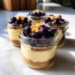 Four individual Lemon Blueberry Cheesecake Jars layered with graham cracker crust, creamy filling, and topped with blueberries.