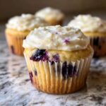 A close-up of a single Lemon Blueberry Cupcake topped with thick cream cheese frosting, sitting on a marble counter.