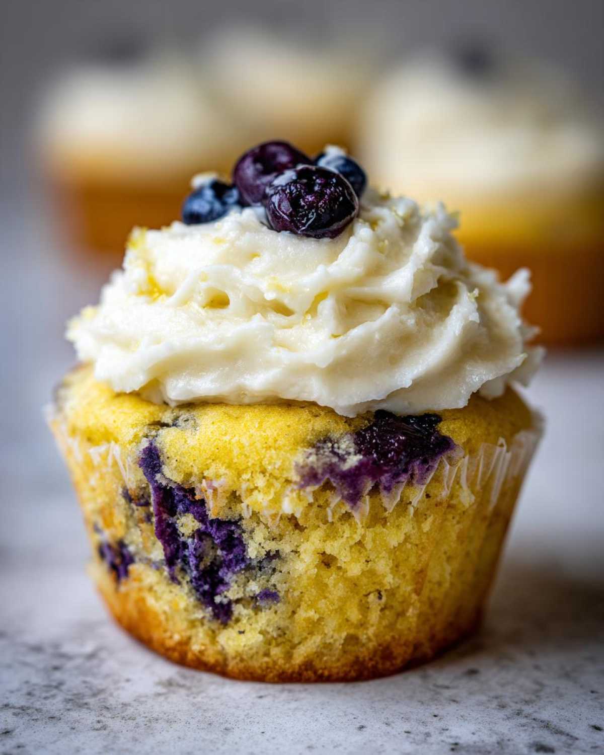 A close-up of a single Lemon Blueberry Cupcake with Cream Cheese Frosting topped with fresh blueberries.