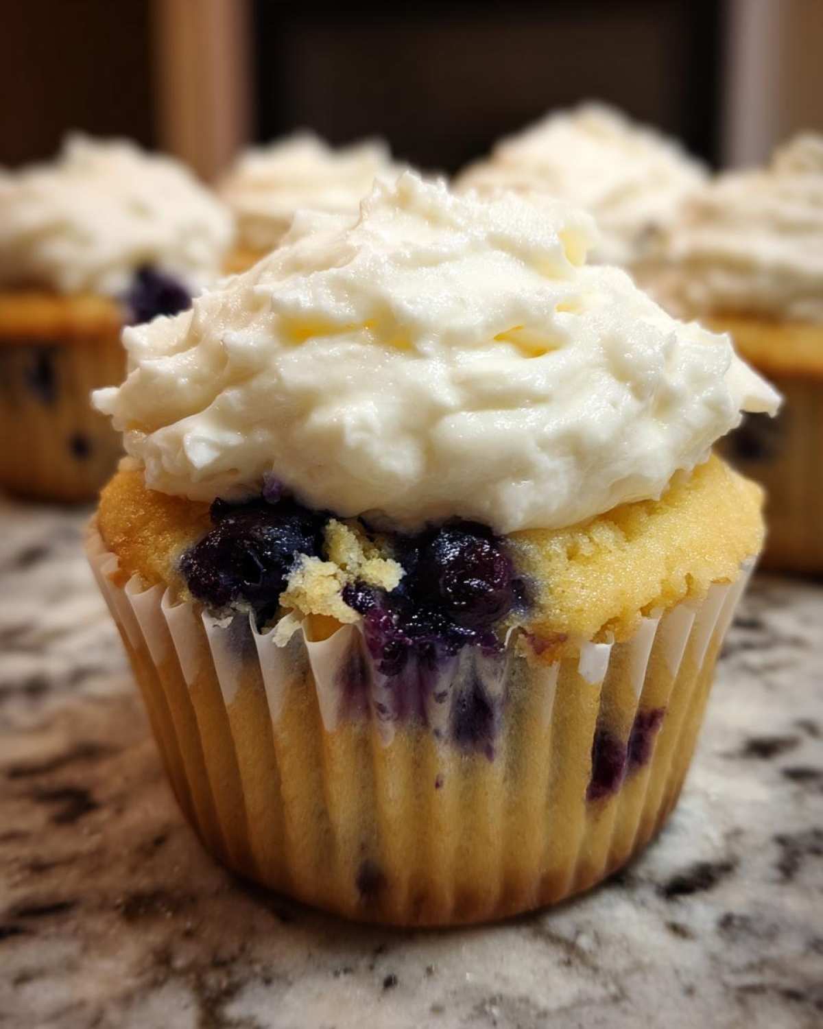 A close-up of a freshly baked Lemon Blueberry Cupcake topped with thick cream cheese frosting.
