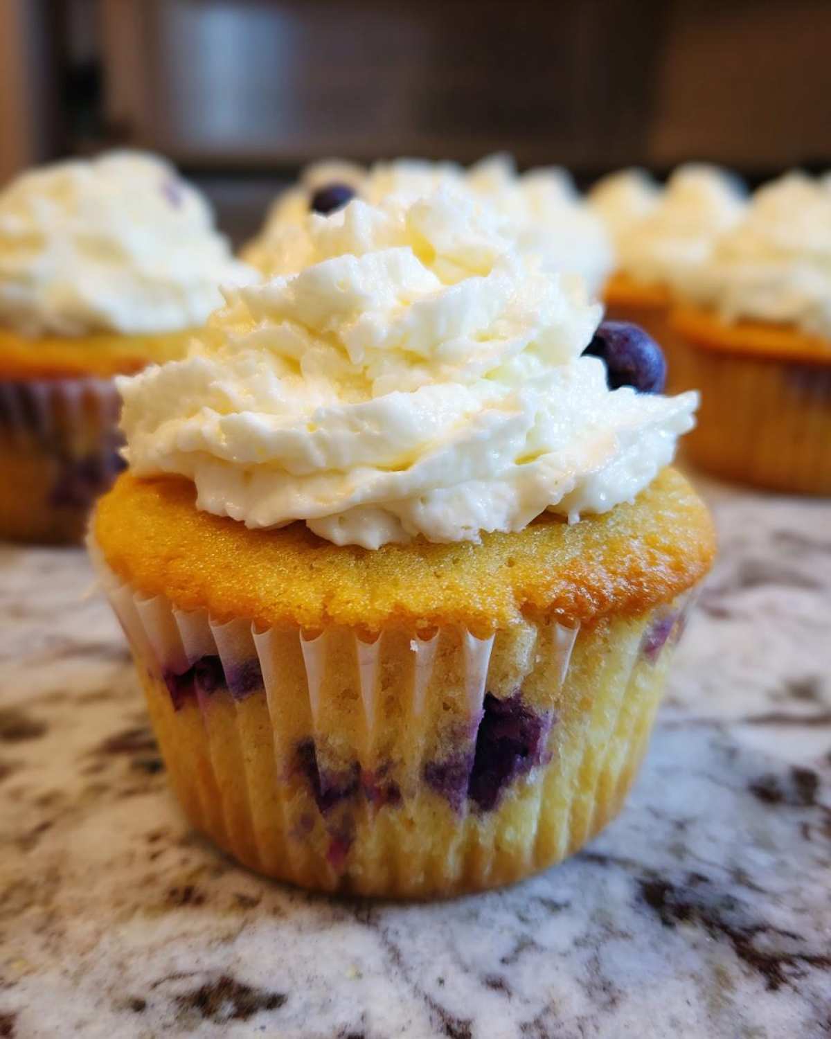 Close-up of a Lemon Blueberry Cupcake with Cream Cheese Frosting, showing blueberries baked into the cake.