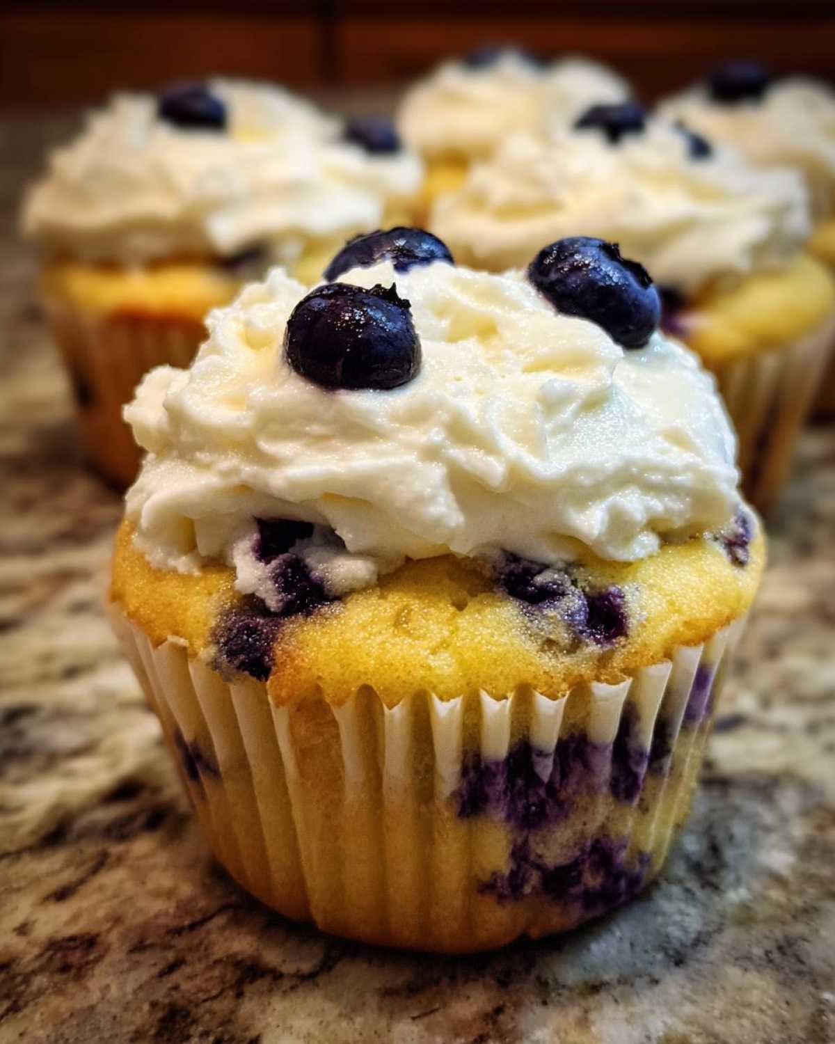 A close-up of a finished Lemon Blueberry Cupcake topped with cream cheese frosting and fresh blueberries.