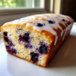 Close-up of a freshly baked Lemon Blueberry Yogurt Loaf drizzled with white lemon glaze and studded with blueberries.