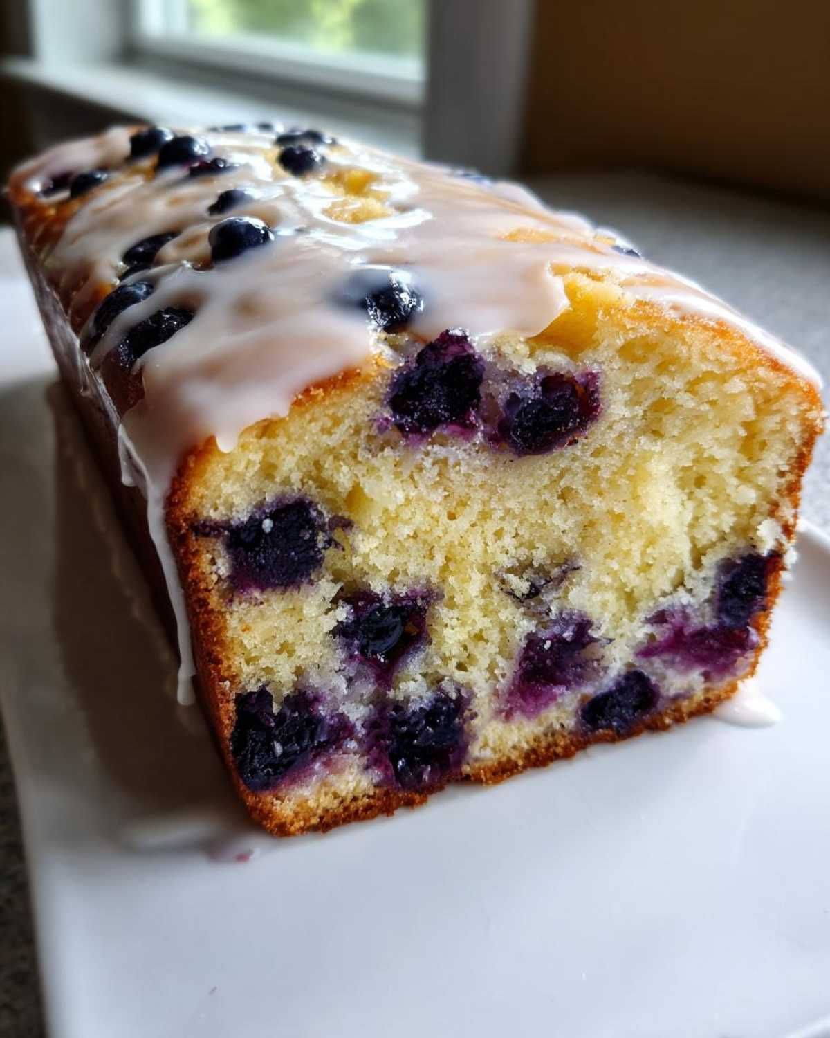 A close-up of a freshly baked Lemon Blueberry Yogurt Loaf drizzled with white icing.