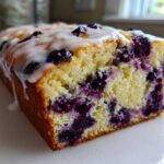 Close-up of a slice of Lemon Blueberry Yogurt Loaf showing moist crumb and fresh blueberries, topped with white glaze.