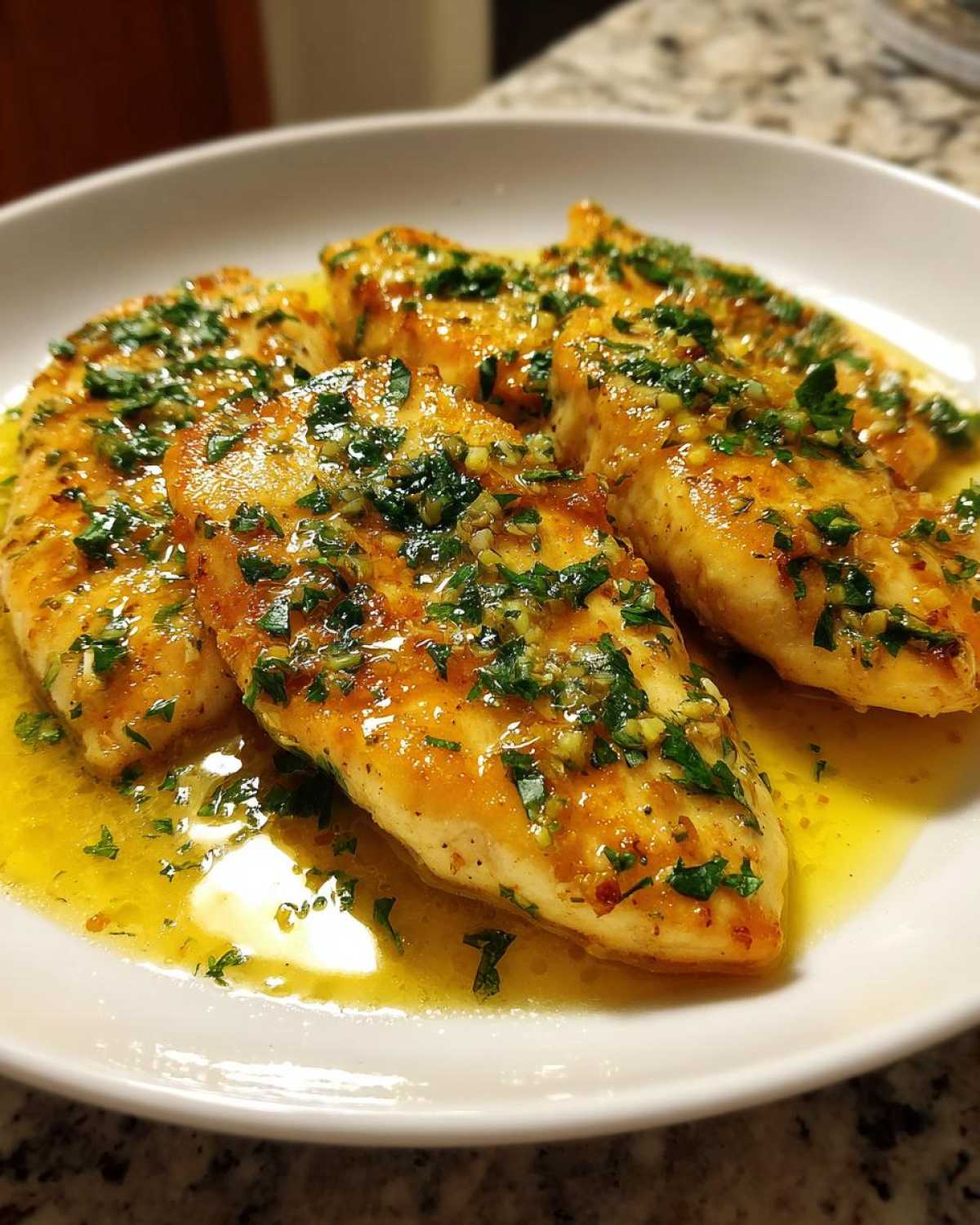 Four fillets of Lemon Garlic Butter Tilapia swimming in a bright, buttery sauce topped with chopped parsley and garlic.