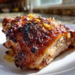 Close-up of a perfectly cooked Lemon Garlic Roasted Chicken Thighs with caramelized, crispy skin and visible garlic pieces.
