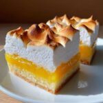Two squares of Lemon Meringue Pie Bars featuring a thick, toasted meringue topping over bright yellow lemon filling and a shortbread crust.