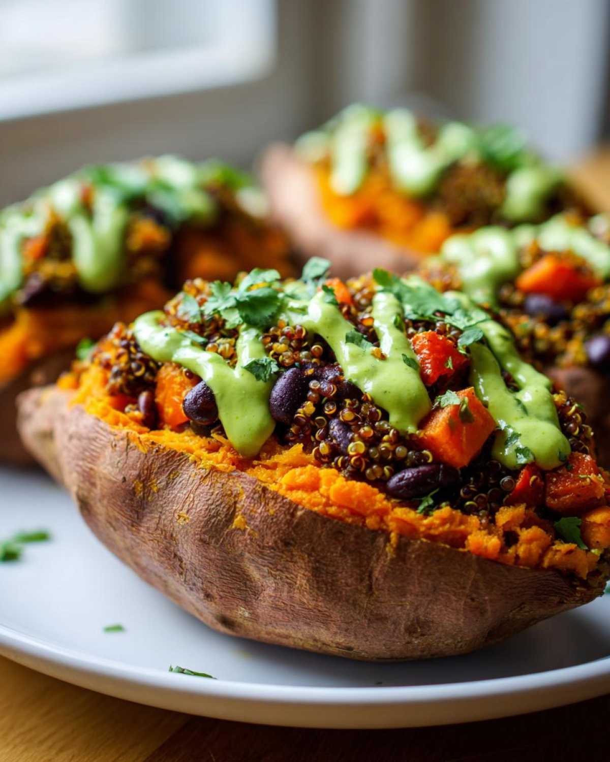 A close-up of one of the Loaded Veggie Stuffed Sweet Potatoes, topped with quinoa, beans, and a bright green sauce.