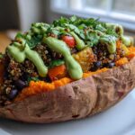 A close-up of one of the Loaded Veggie Stuffed Sweet Potatoes, topped with quinoa, black beans, and a drizzle of green sauce.