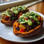 Two Loaded Veggie Stuffed Sweet Potatoes filled with quinoa, black beans, and topped with a bright green sauce and cilantro.