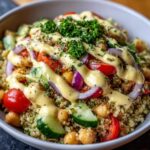 Close-up of a vibrant Mediterranean Quinoa Bowl topped generously with lemon tahini sauce, chickpeas, tomatoes, and red onion.