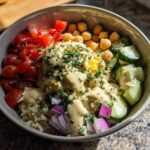 A vibrant Mediterranean Quinoa Bowl featuring quinoa, chickpeas, tomatoes, cucumbers, red onion, and generous lemon tahini sauce.
