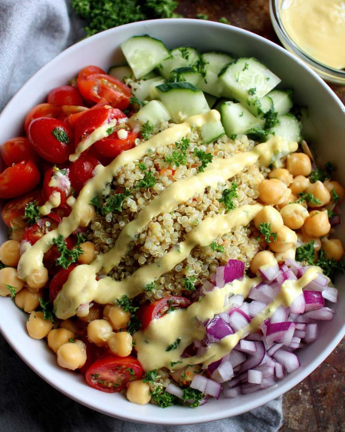 Close-up of a vibrant Mediterranean Quinoa Bowl topped with chickpeas, tomatoes, cucumbers, red onion, and lemon tahini sauce.