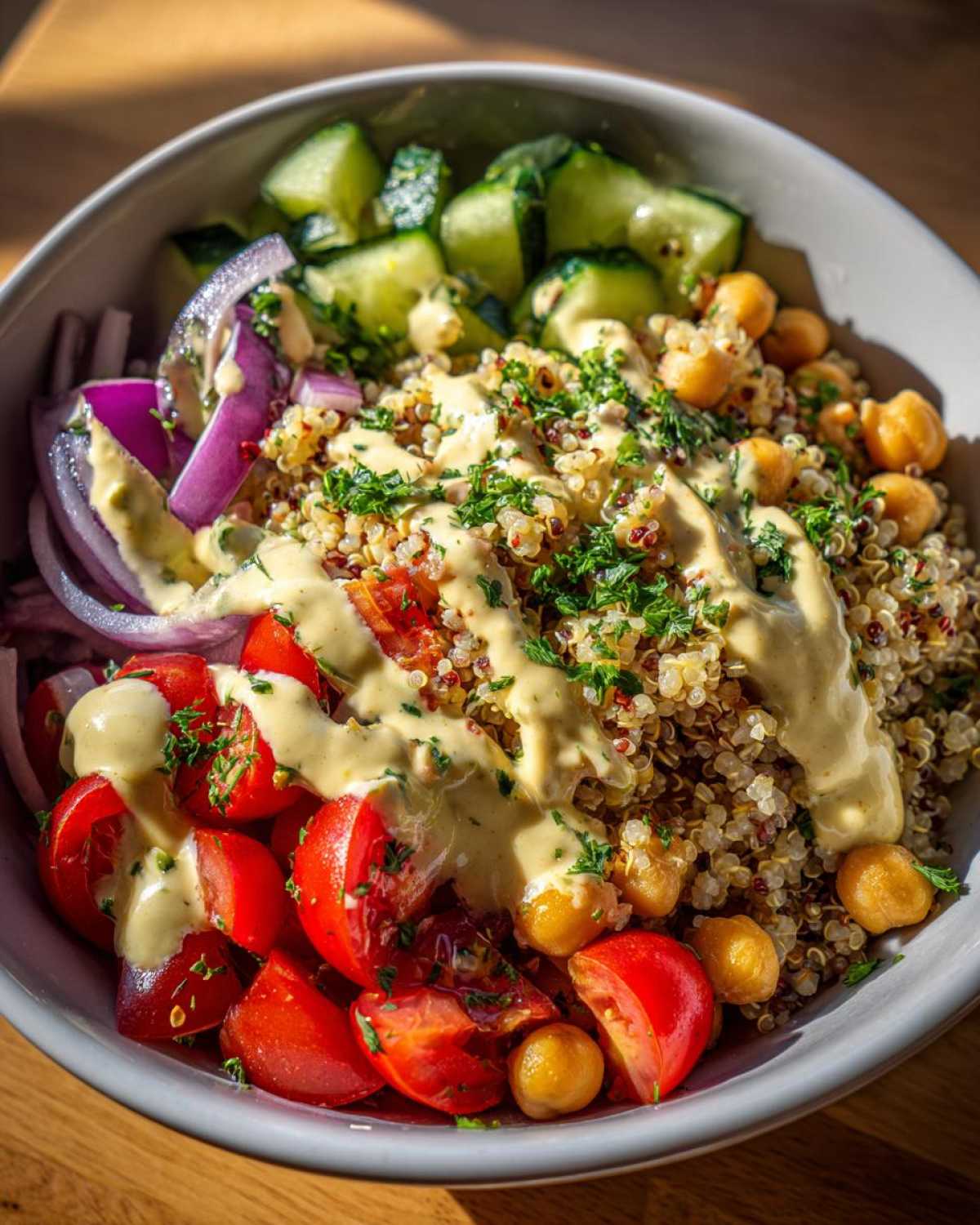 Close-up of a vibrant Mediterranean Quinoa Bowl with Lemon Tahini Sauce drizzled over quinoa, tomatoes, cucumbers, and chickpeas.