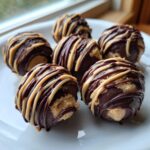 Close-up of several No-Bake Chocolate Covered Banana Bites drizzled with peanut butter on a white plate.