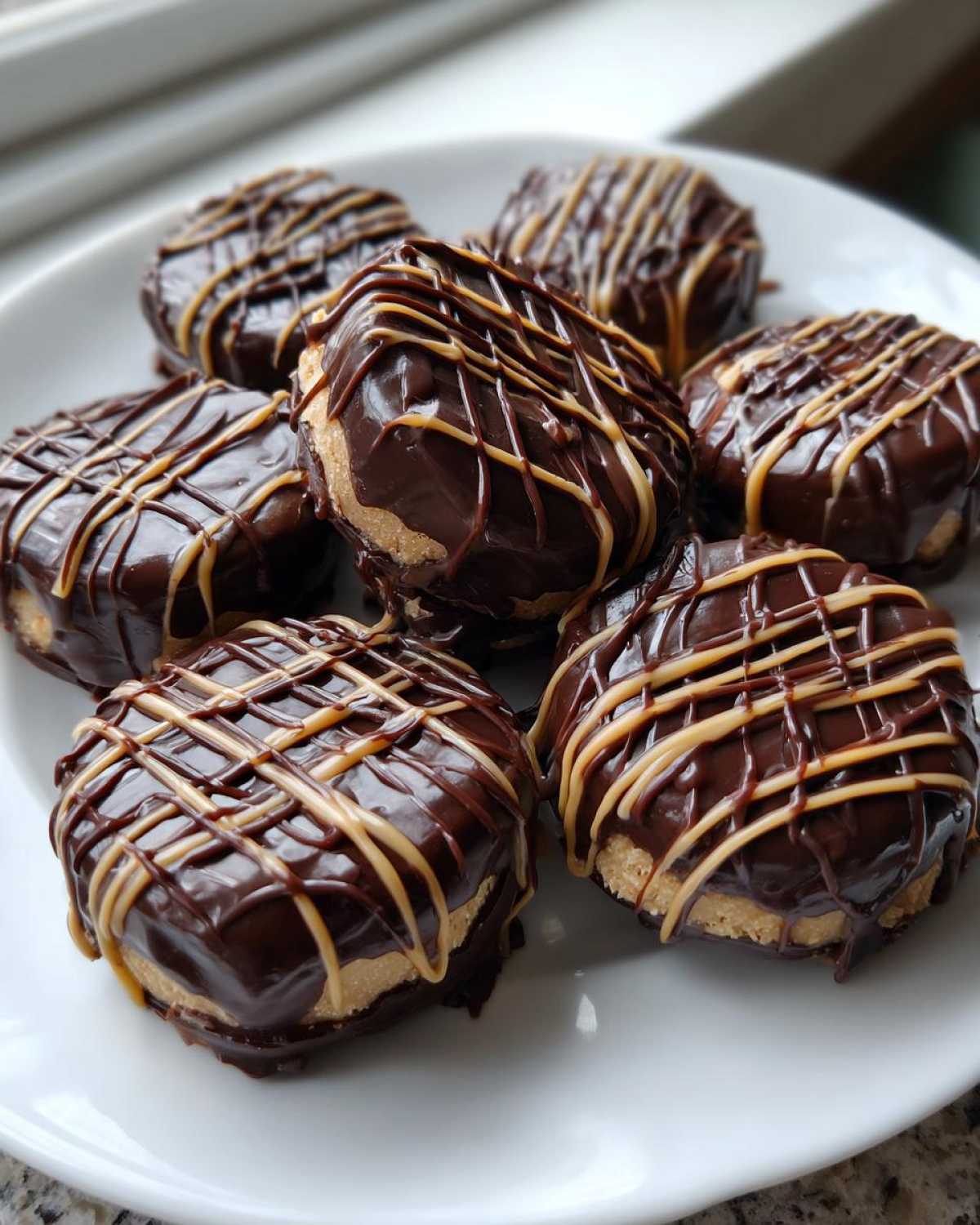 Close-up of several No-Bake Chocolate Covered Banana Bites drizzled with peanut butter on a white plate.