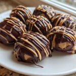 Close-up of several No-Bake Chocolate Covered Banana Bites drizzled with peanut butter on a white plate.