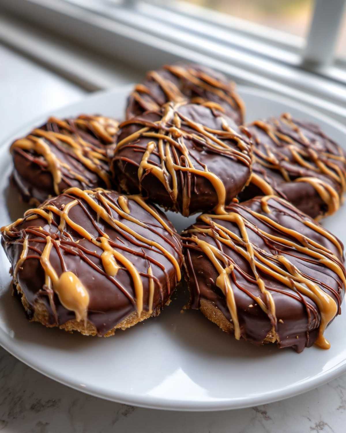 Close-up of several No-Bake Chocolate Covered Banana Bites drizzled with peanut butter on a white plate.