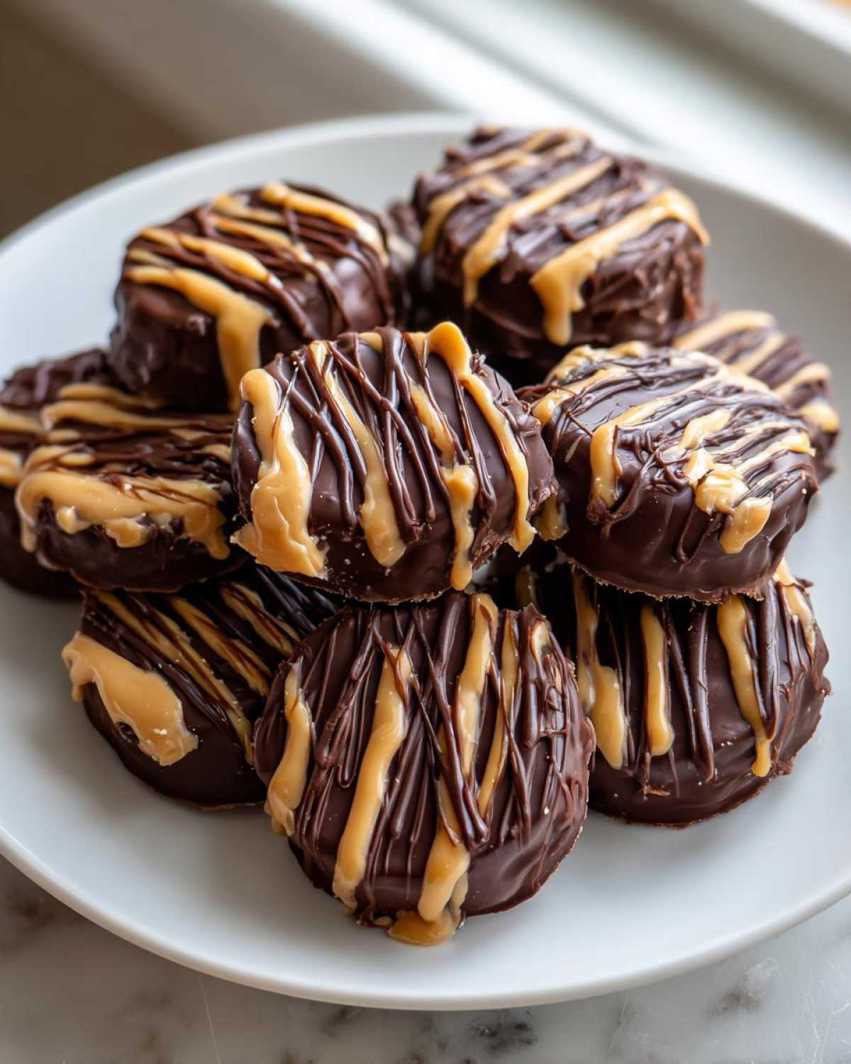 A stack of delicious No-Bake Chocolate Covered Banana Bites drizzled with peanut butter or caramel on a white plate.