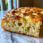 Close-up of the airy, open crumb texture of No-Knead Skillet Focaccia with Rosemary, showing a golden crust.