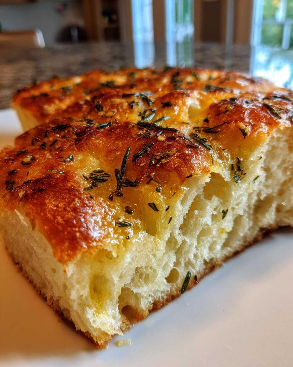 Close-up of a fluffy slice of No-Knead Skillet Focaccia with Rosemary, showing the airy crumb and golden, oily top.