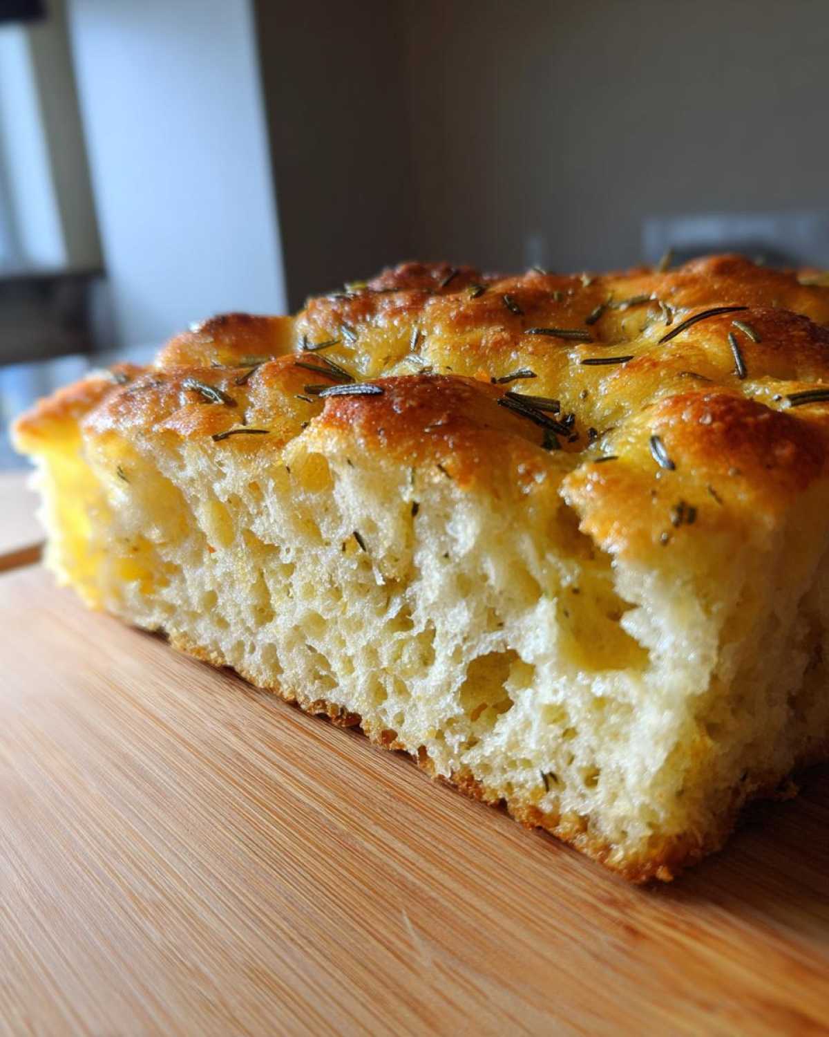 A thick slice showing the airy crumb structure of No-Knead Skillet Focaccia with Rosemary on a wooden cutting board.