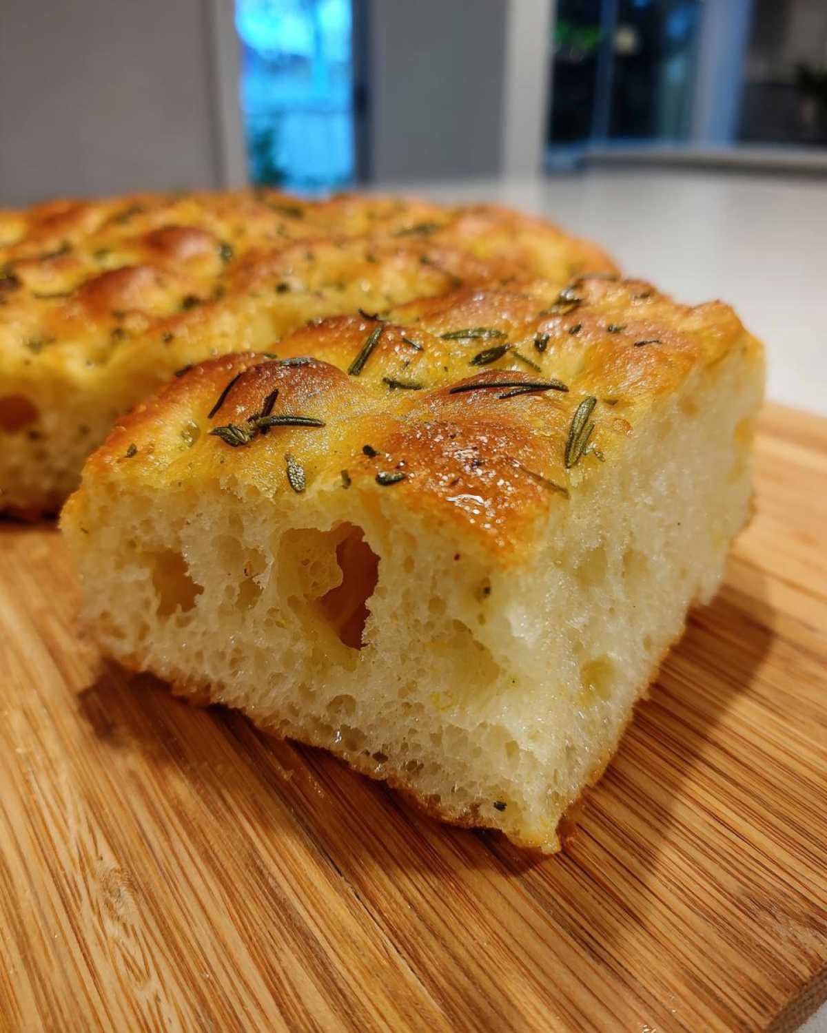 Close-up of a thick, airy slice of No-Knead Skillet Focaccia with Rosemary on a wooden board.