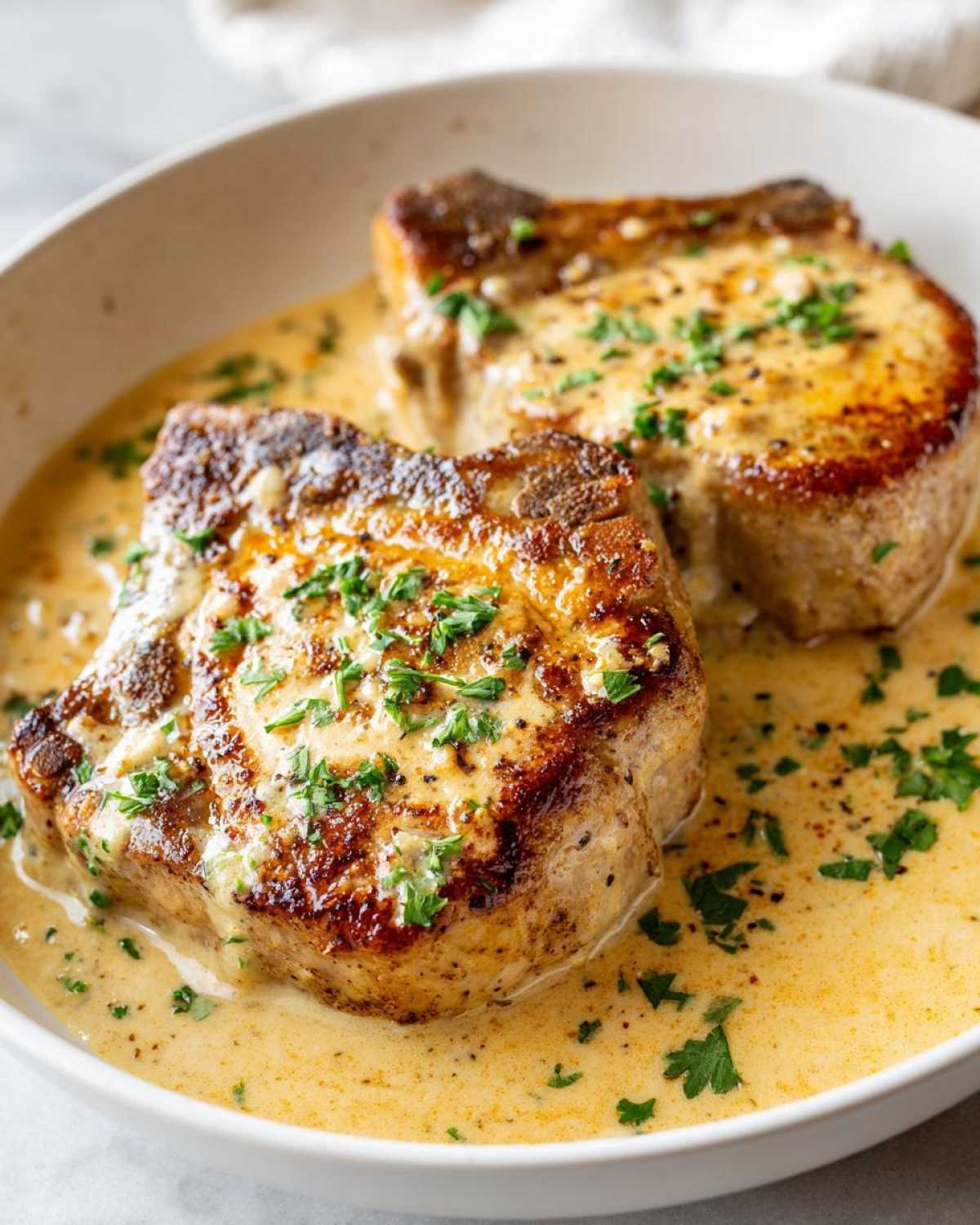 Two seared One-Pan Creamy Garlic Pork Chops covered in a rich, creamy garlic sauce and garnished with fresh parsley.