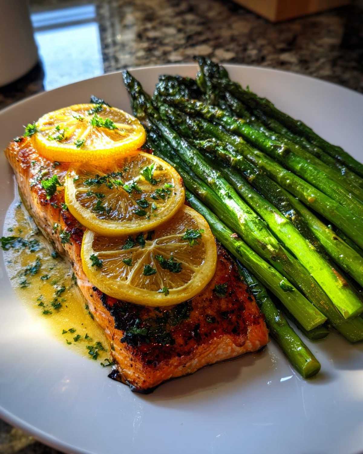 A perfectly cooked fillet of One-Pan Lemon Garlic Salmon served with roasted asparagus spears and lemon slices.