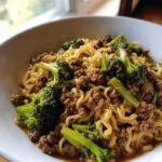 A close-up serving of One-Pot Beef and Broccoli Ramen Noodles mixed with ground beef and bright green broccoli florets in a white bowl.