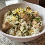 A close-up of a white bowl filled with One-Pot Chicken and Rice with Lemon Herbs, topped with fresh parsley and lemon zest.