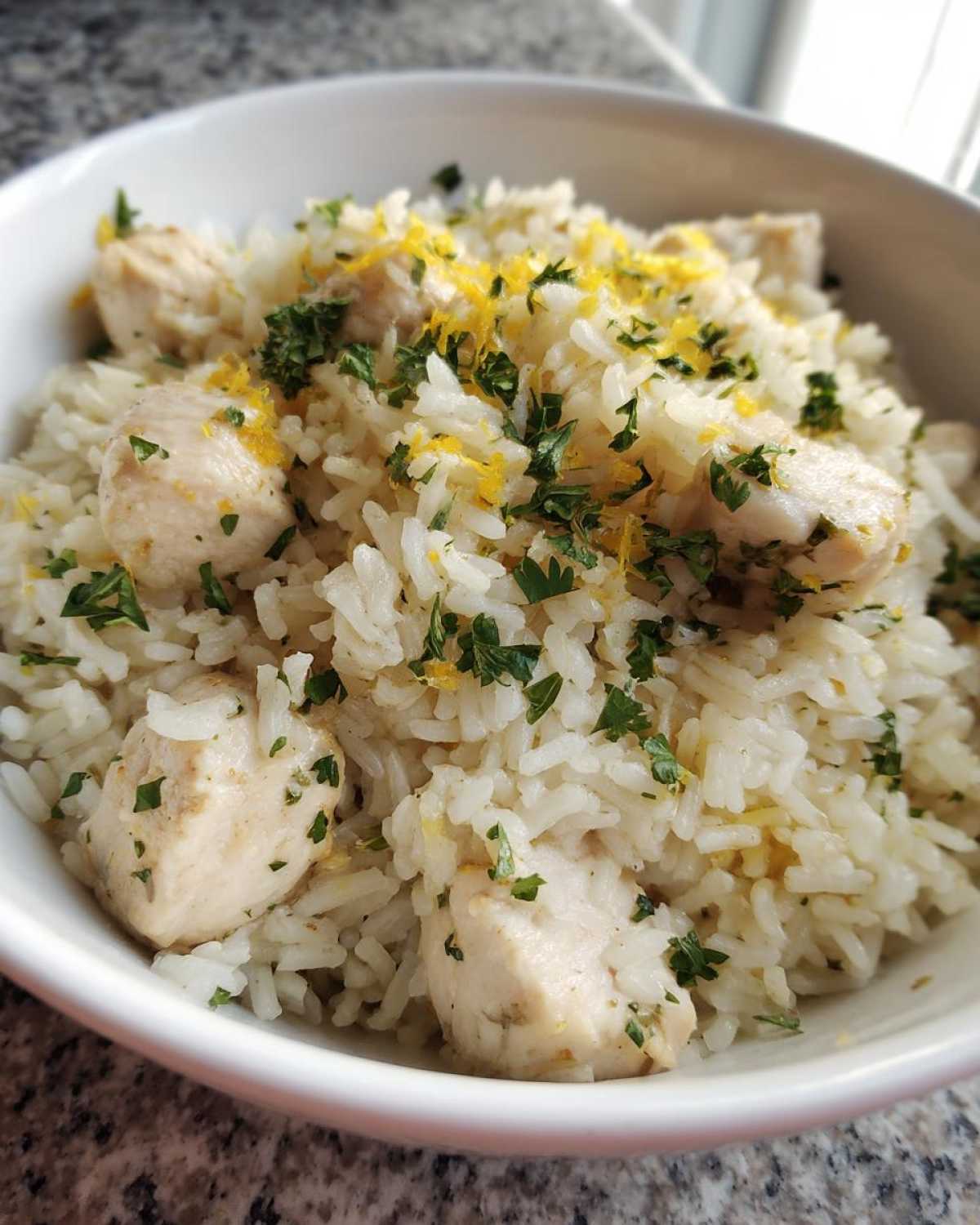 A close-up of One-Pot Chicken and Rice with Lemon and Herbs, topped with fresh parsley and lemon zest.
