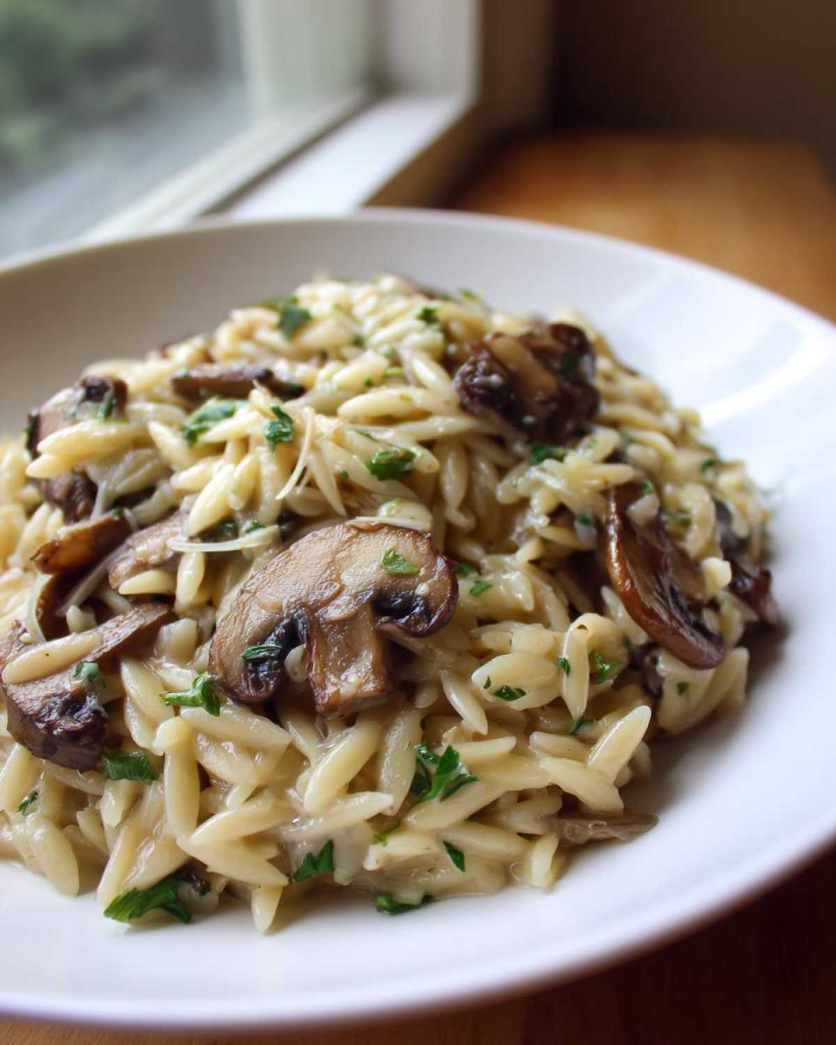 A close-up of a white bowl filled with One-Pot Creamy Mushroom Orzo, topped with sautéed mushrooms and parsley.