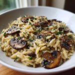 A close-up of a white bowl filled with creamy One-Pot Creamy Mushroom Orzo, topped with sautéed mushrooms and parsley.