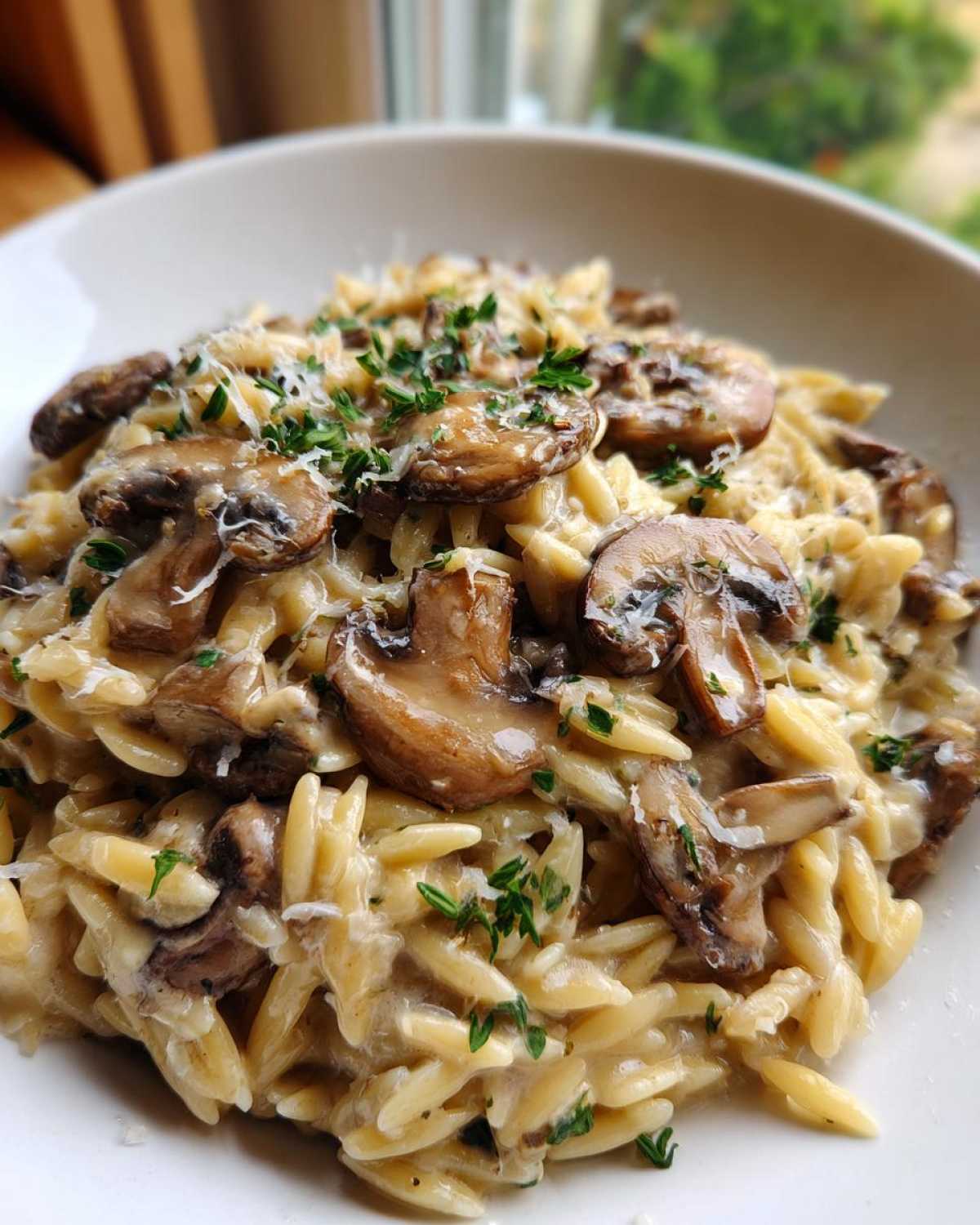 A close-up of a serving of One-Pot Creamy Mushroom Orzo topped with sliced sautéed mushrooms and fresh parsley.