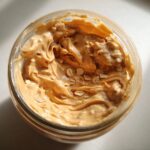 Overhead view of creamy peanut butter swirled into a jar, showing visible oat flakes for High-Protein Peanut Butter Overnight Oats.