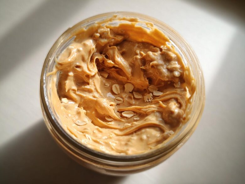 Overhead view of creamy peanut butter swirled into a jar, showing visible oat flakes for High-Protein Peanut Butter Overnight Oats.