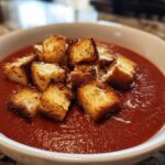 A close-up of rich red Roasted Tomato Basil Soup topped with golden Grilled Cheese Croutons.