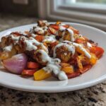 A serving of Sheet Pan Chicken Shawarma with roasted peppers and onions, drizzled generously with garlic yogurt sauce.
