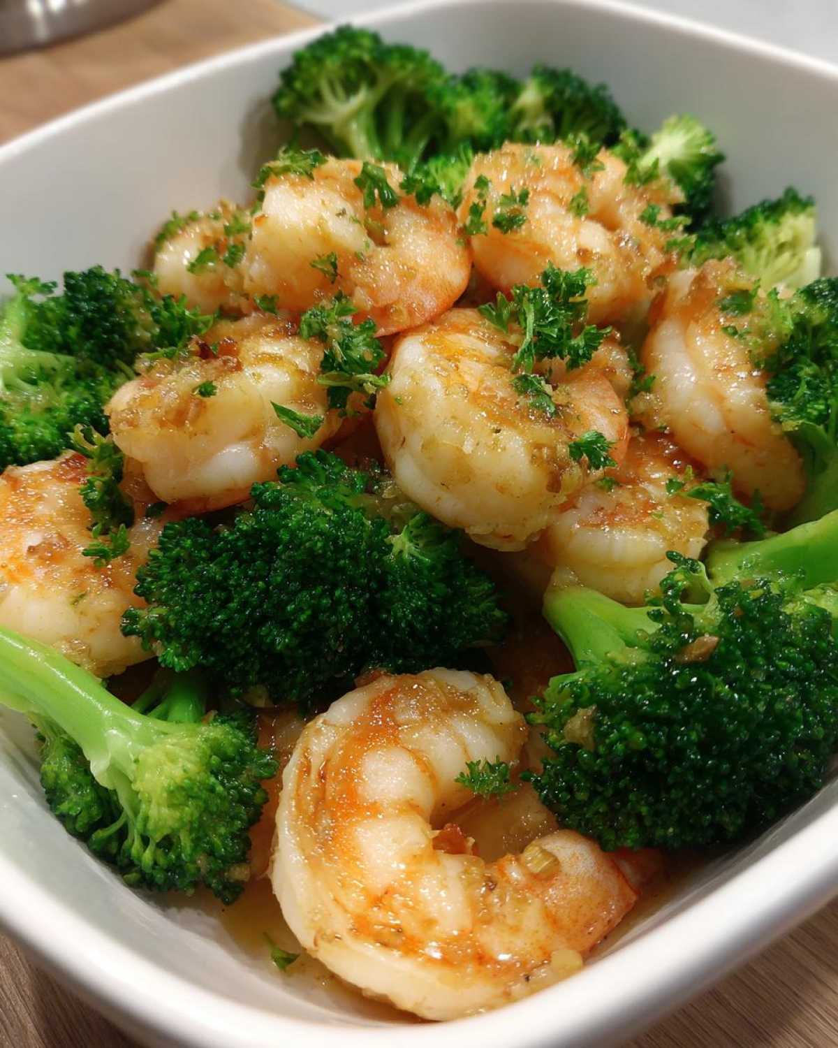 Close-up of cooked shrimp coated in garlic butter sauce mixed with bright green broccoli florets.