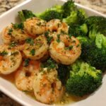 Close-up of cooked shrimp coated in garlic butter sauce served with bright green broccoli florets.