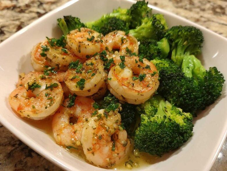 Close-up of cooked shrimp coated in garlic butter sauce served with bright green broccoli florets.