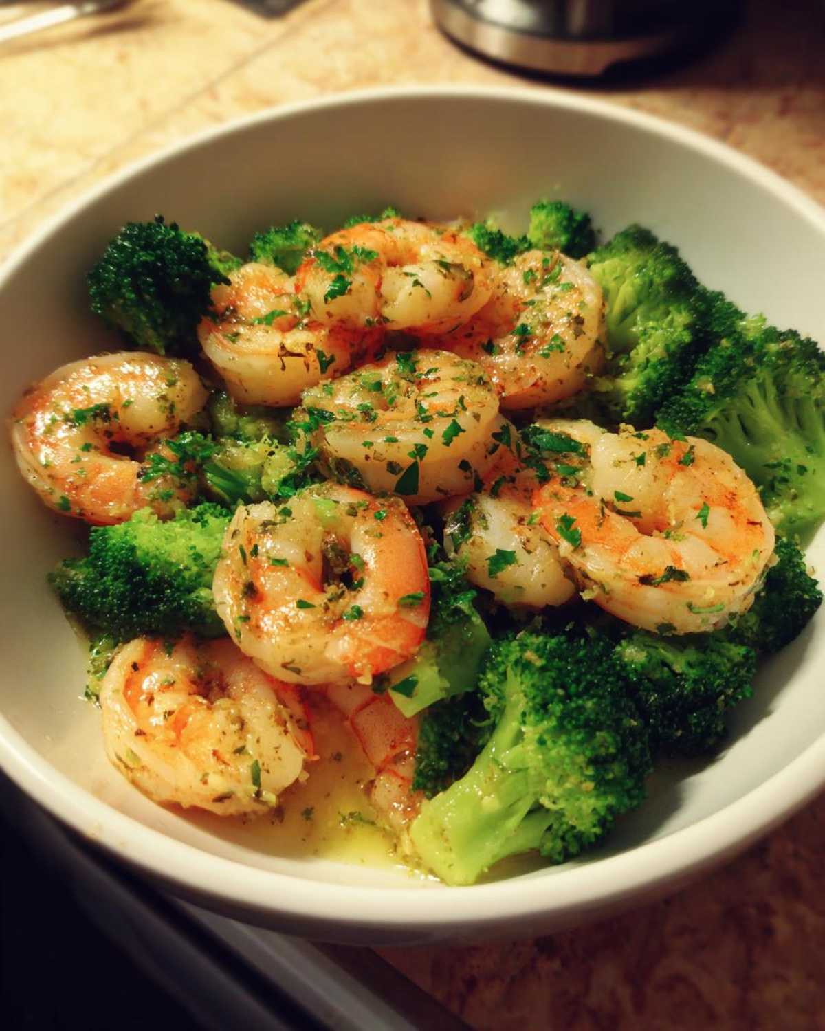 Close-up of cooked shrimp and bright green broccoli florets tossed in garlic butter sauce, ready to eat.