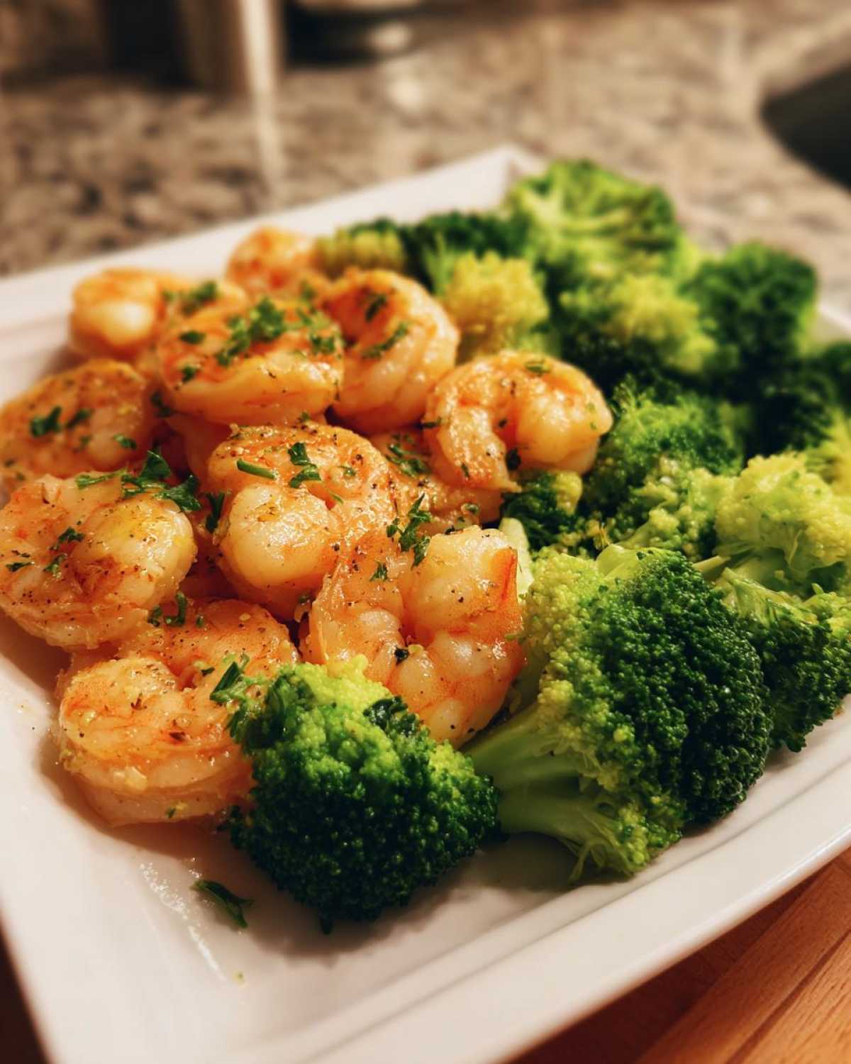 A close-up of cooked shrimp and bright green broccoli florets served on a white plate, seasoned for Sheet Pan Garlic Butter Shrimp and Broccoli.