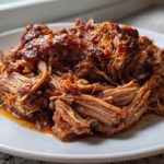 Close-up of tender, shredded Slow Cooker Honey Garlic Pulled Pork coated in a rich, glossy sauce on a white plate.