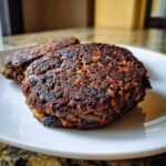 A close-up of a richly browned and seared Smoky Black Bean Burger Patty resting on a white plate.
