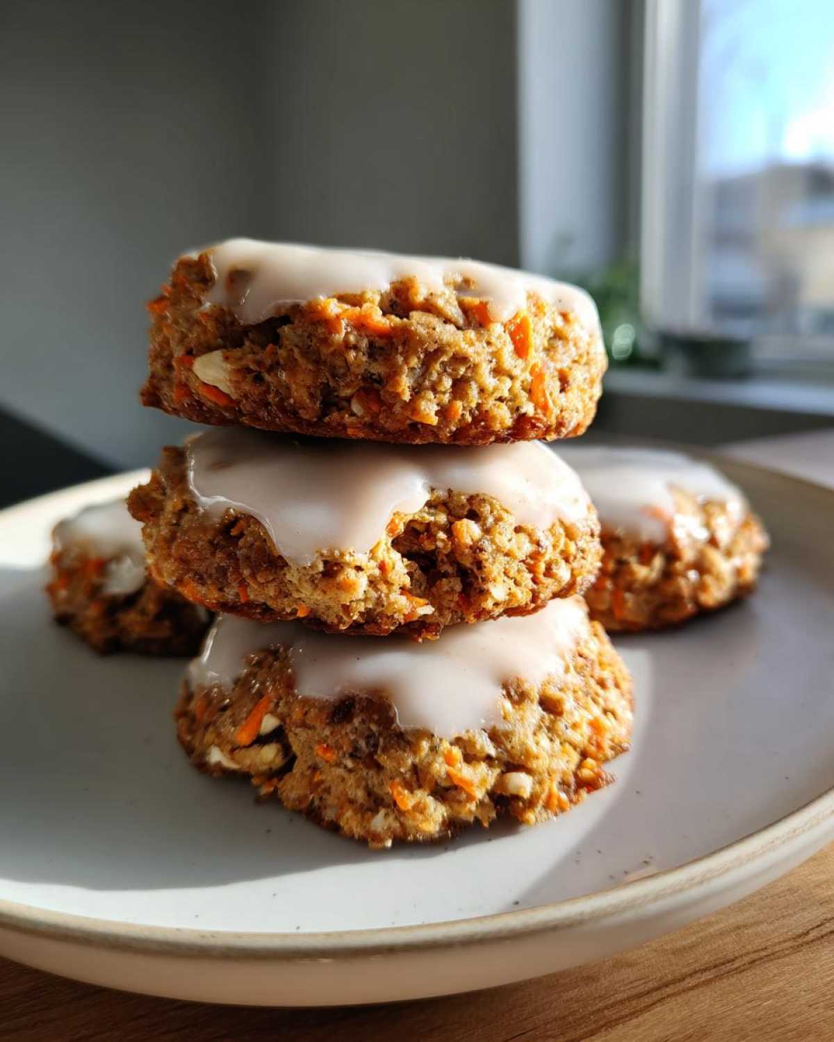 A stack of three Soft-Baked Carrot Cake Cookies topped with a thick cream cheese glaze on a light plate.