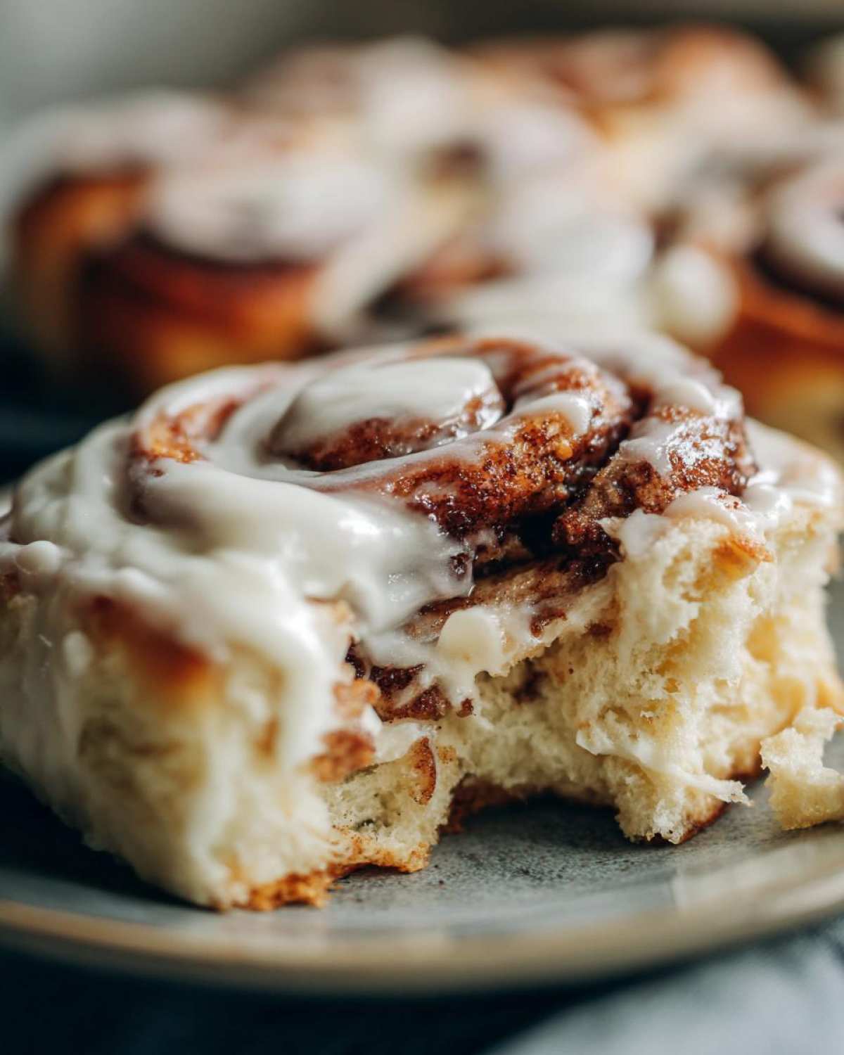 A soft, gooey Gluten-Free Cinnamon Roll with a bite taken out, covered in thick white icing.