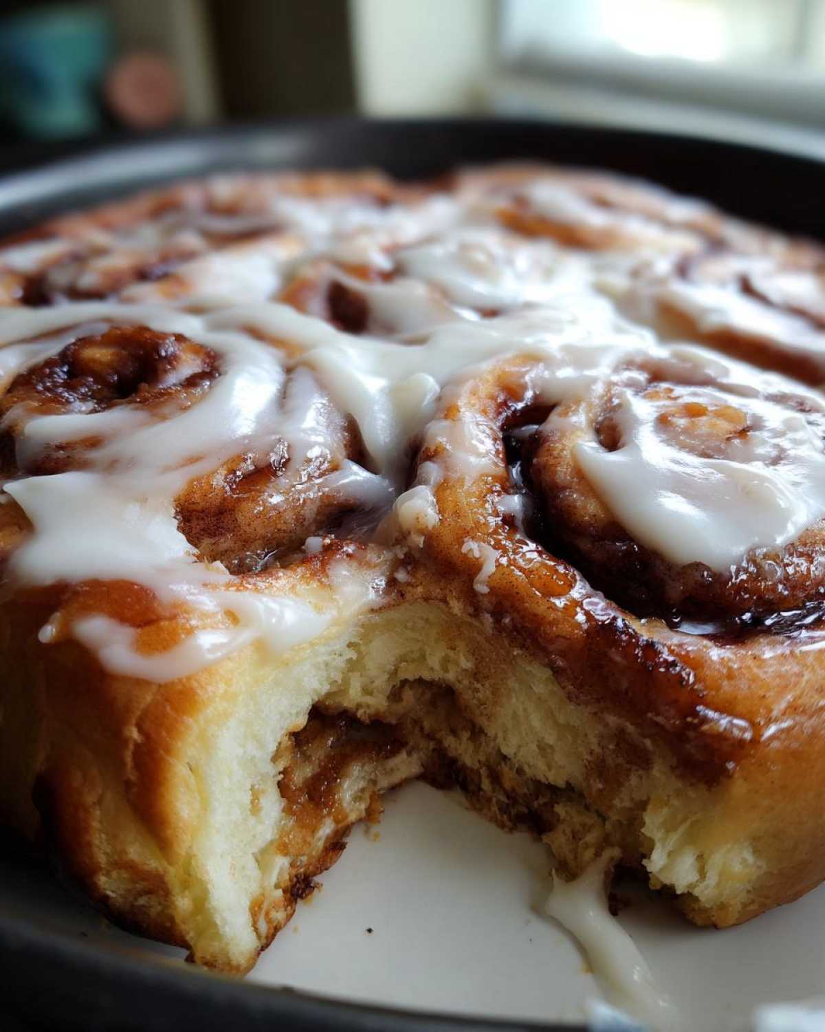 Close-up of soft Gluten-Free Cinnamon Rolls, one piece taken out, dripping with white icing.